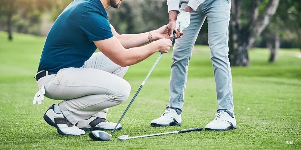 one person squatting on a golf course while another person holds a golf club.